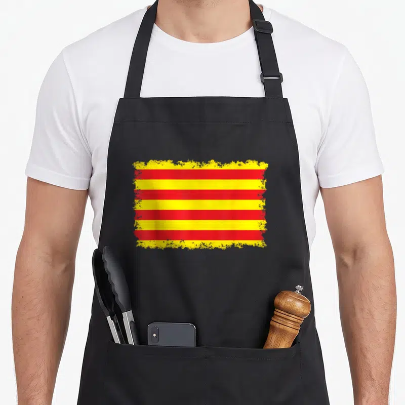 Tablier de cuisine noir avec le drapeau catalan aux bandes rouges et jaunes aux bords estompés.