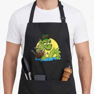 Tablier de cuisine noir avec un monstre du Loch Ness vert portant un bonnet tartan et jouant de la cornemuse.