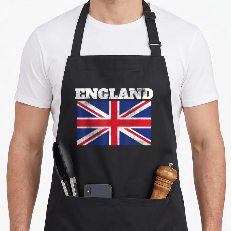 Tablier de cuisine noir avec le drapeau England et texte blanc délavé au centre.