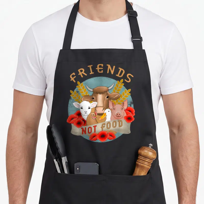 Tablier de cuisine noir avec illustration d'animaux et texte Friends Not Food entouré de fleurs rouges.