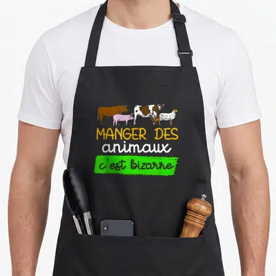 Tablier de cuisine noir avec inscription Manger des animaux c'est bizarre et dessin de vaches et moutons colorés.