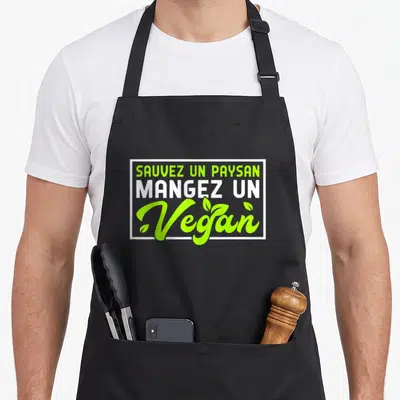 Tablier de cuisine noir avec l'inscriptionSauvez un paysan mangez un vegan en vert et blanc encadrée de blanc.