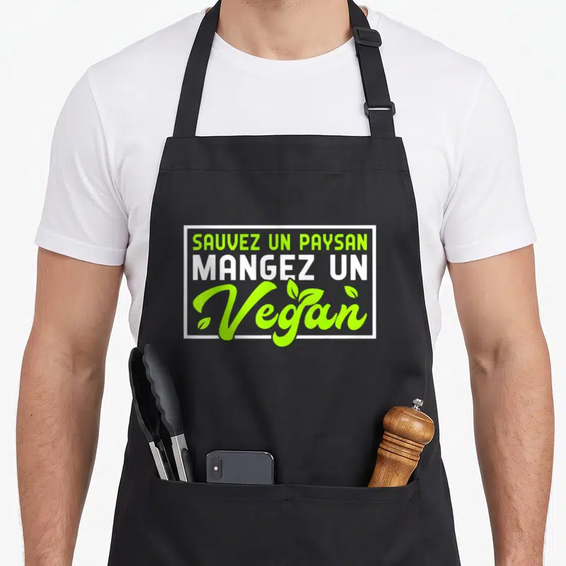 Tablier de cuisine noir avec l'inscriptionSauvez un paysan mangez un vegan en vert et blanc encadrée de blanc.