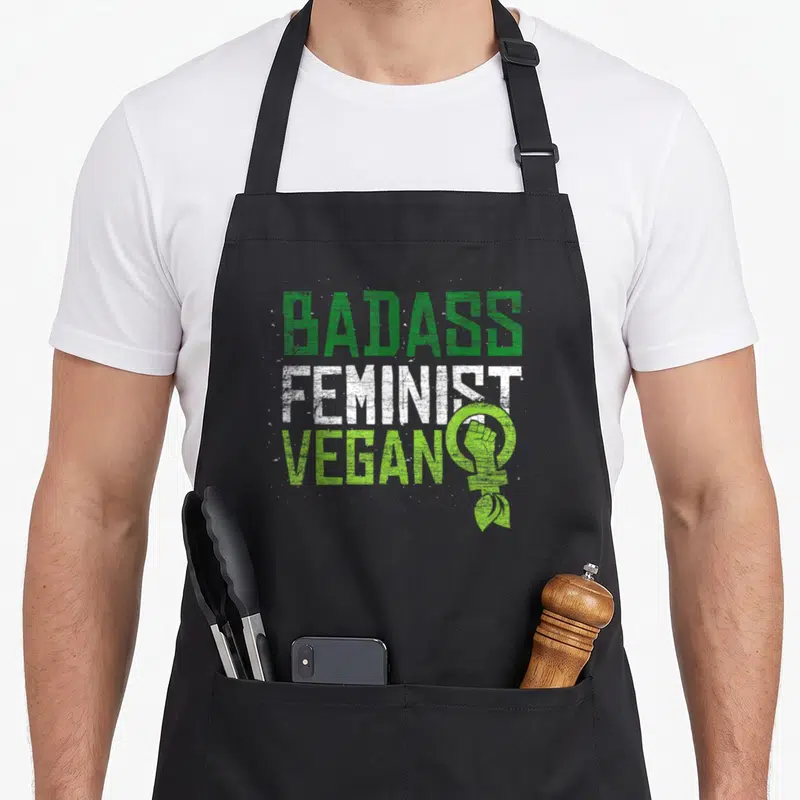 Tablier de cuisine noir avec linscription Badass Feminist Vegan et un poing levé dans le signe féminin vert