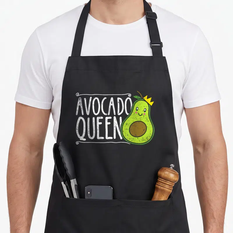 Tablier de cuisine noir avec illustration d'un avocat souriant portant une couronne jaune et le texte Avocado Queen en lettres blanches.
