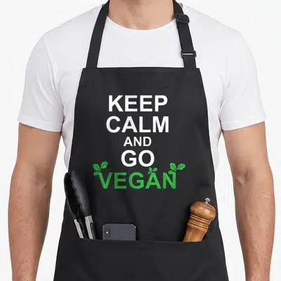 Tablier de cuisine noir avec l'inscription Keep Calm and Go Vegan en blanc et vert surmonté de petites feuilles.