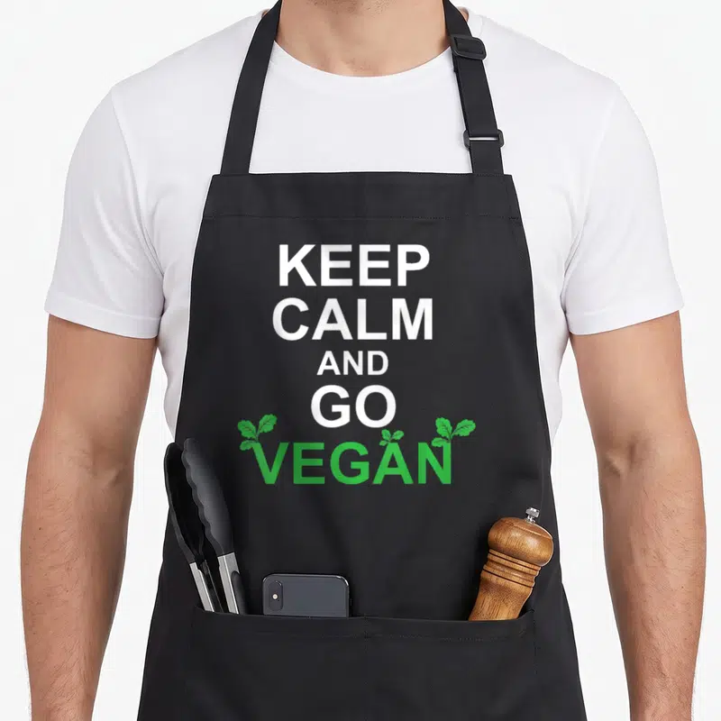Tablier de cuisine noir avec l'inscription Keep Calm and Go Vegan en blanc et vert surmonté de petites feuilles.