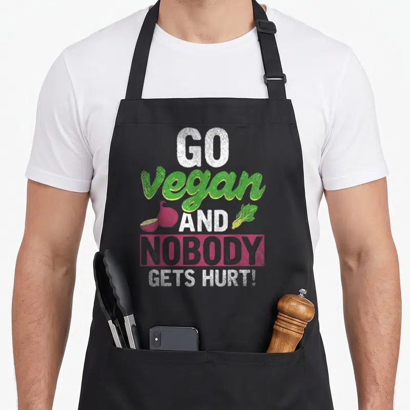 Tablier de cuisine noir avec l'inscription Go vegan and nobody gets hurt accompagnée d'une illustration de légumes colorés.