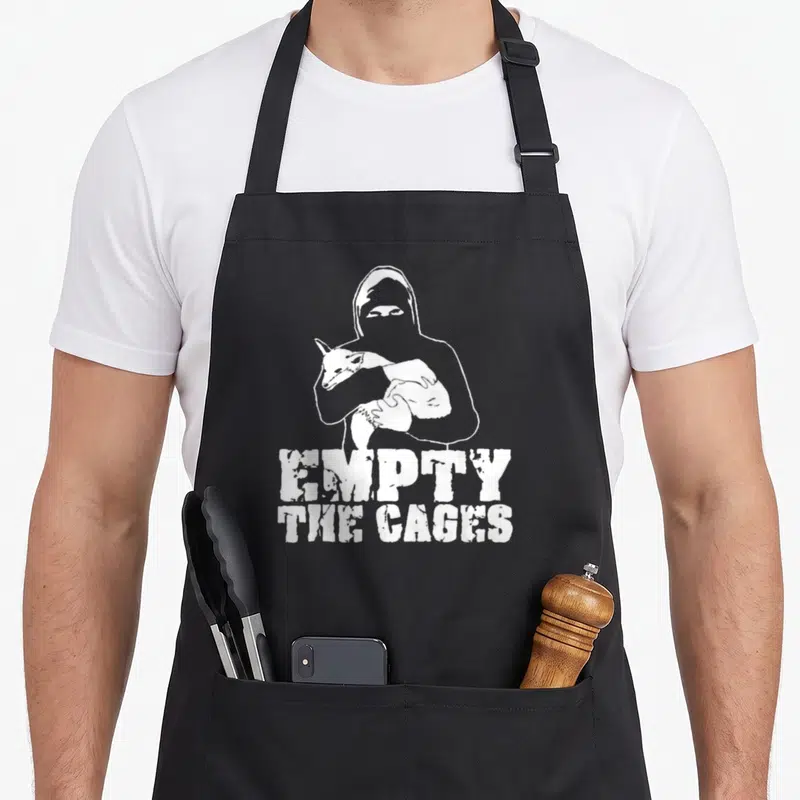 Tablier de cuisine noir avec silhouette masquée tenant un animal et texte Empty The Cages en blanc.