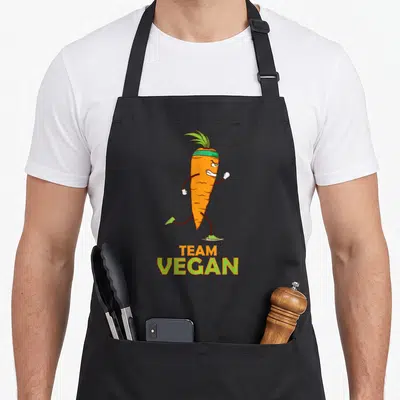 Tablier de cuisine noir avec une carotte orange courant en bandes dessinées et l'inscription Team Vegan.