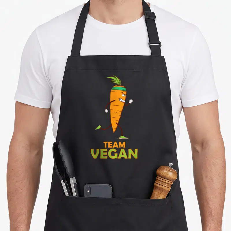Tablier de cuisine noir avec une carotte orange courant en bandes dessinées et l'inscription Team Vegan.