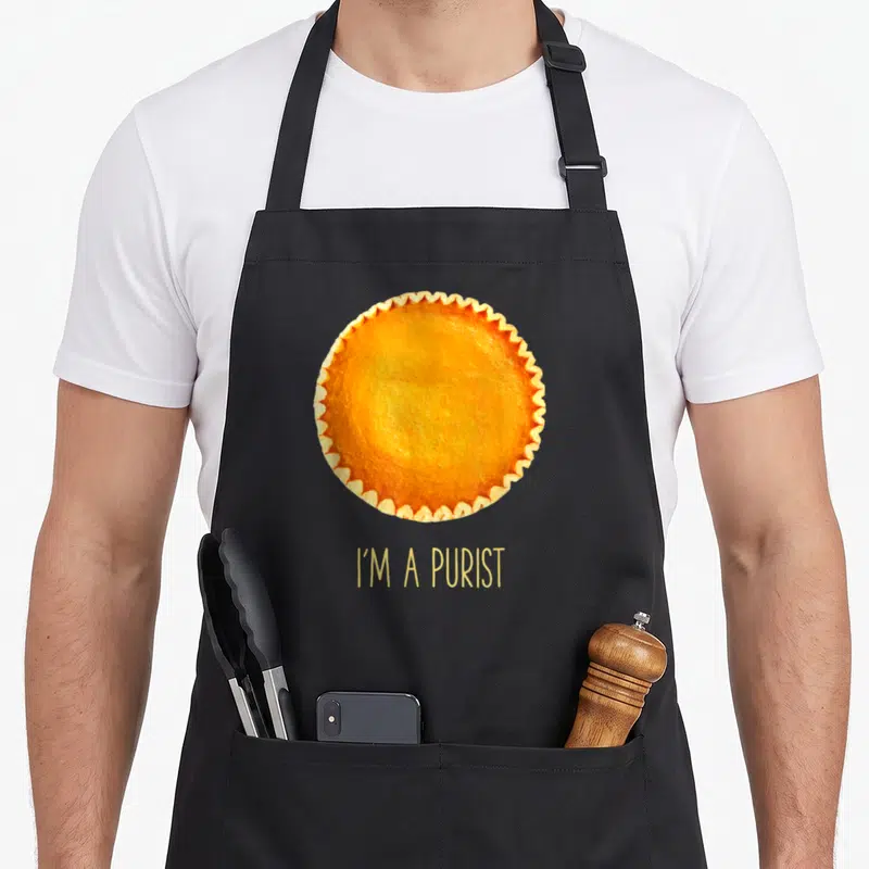 Tablier de cuisine noir avec une tarte aux pommes orange et le texte I'm a purist en jaune.