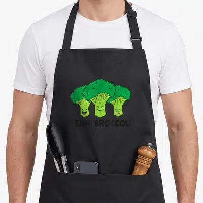 Tablier de cuisine noir avec trois brocolis animés et l'inscription Team Broccoli en lettres noires audacieuses.