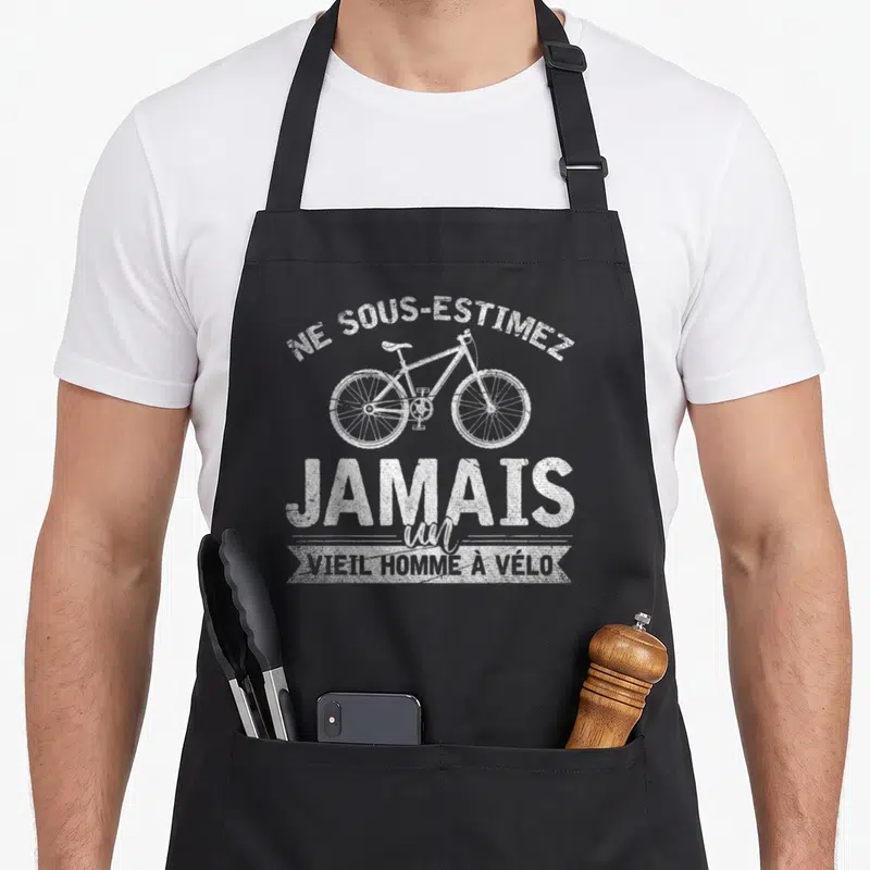 Tablier de cuisine noir avec illustration de vélo blanc et texte humoristique sur fond uni.