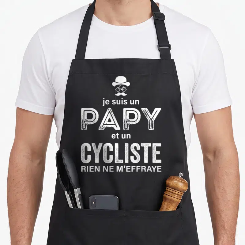 Tablier de cuisine noir avec une illustration de chapeau, moustache et texte blanc soulignant l'identité du cycliste.