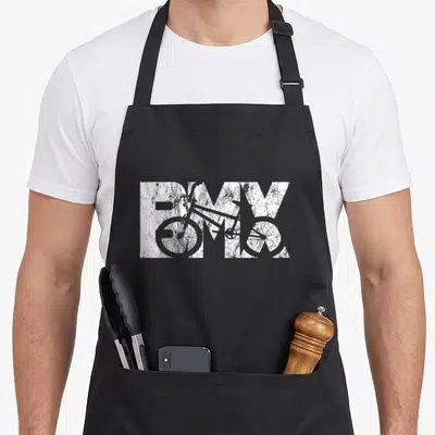 Tablier de cuisine noir avec le texte BMX blanc texturé et une silhouette de vélo vintage intégrée au dessin graphique.