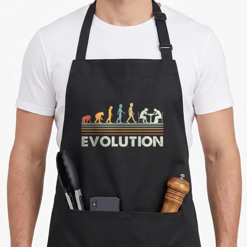 Tablier de cuisine noir avec illustration évolutive colorée et deux joueurs d'échecs assis face à face au-dessus du mot EVOLUTION