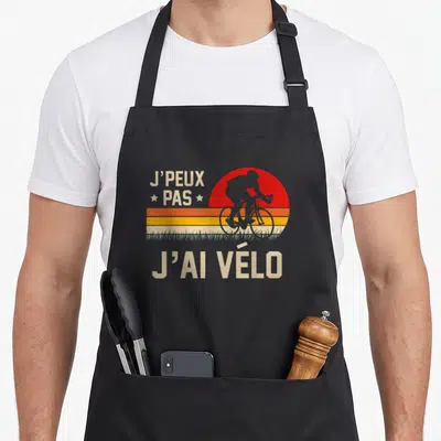 Tablier de cuisine noir avec illustration rétro d'un cycliste devant un soleil rouge et le texte J'peux pas j'ai vélo.