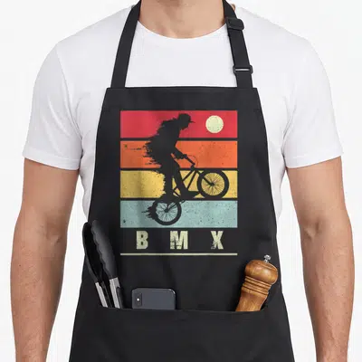 Tablier de cuisine noir avec silhouette cycliste BMX sur bandes colorées et inscription BMX en bas.