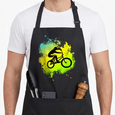 Tablier de cuisine noir avec silhouette cycliste BMX sur fond d'éclaboussures jaune et vert vif.