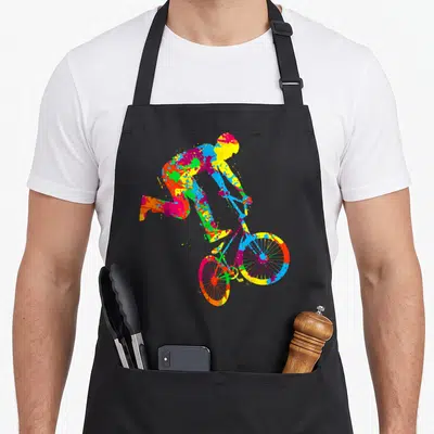 Tablier de cuisine noir avec silhouette colorée d'un cycliste effectuant un saut sur fond uni.