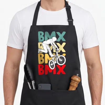 Tablier de cuisine noir avec illustration d'un cycliste BMX blanc devant des lettres colorées.