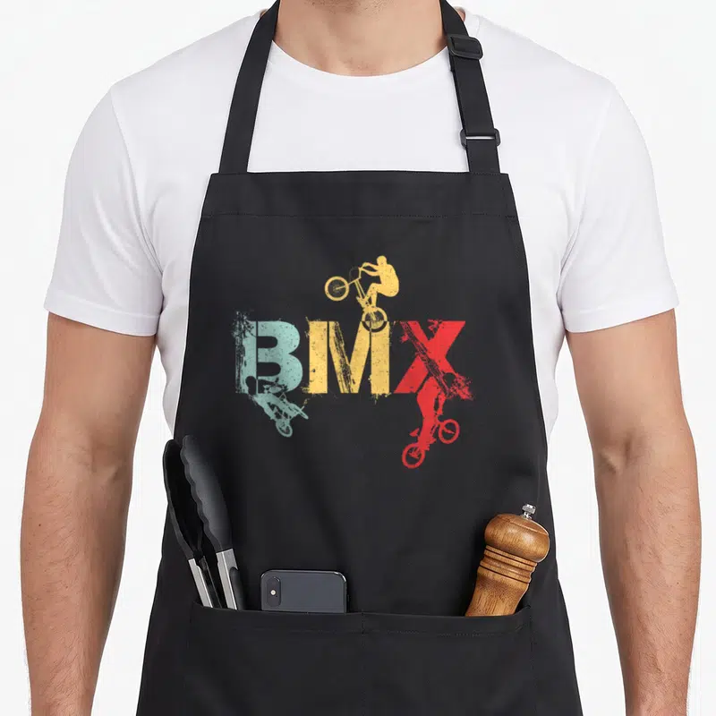 Tablier de cuisine noir avec inscription BMX multicolore et trois silhouettes de cyclistes effectuant des tricks aériens.