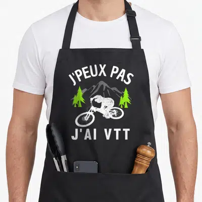 Tablier de cuisine noir avec cycliste VTT blanc, arbres verts et texte J'peux pas j'ai VTT en typographie blanche.