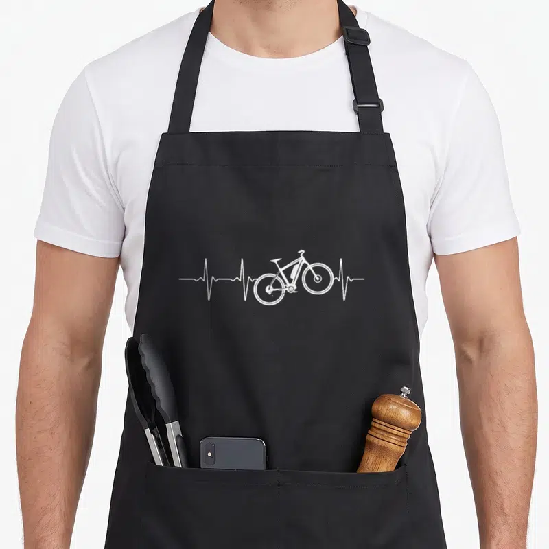 Tablier de cuisine noir avec un motif blanc représentant une ligne de rythme cardiaque traversée par le dessin d'une bicyclette électrique.