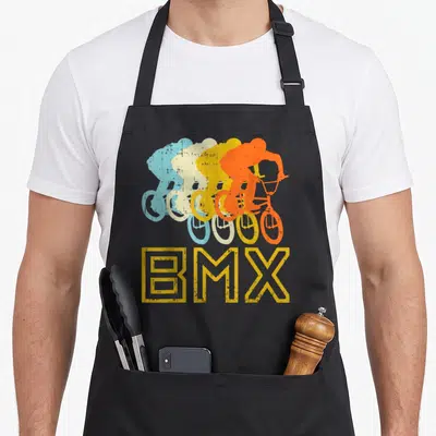 Tablier de cuisine noir avec quatre silhouettes de cyclistes BMX colorées et l'inscription BMX jaune en bas.