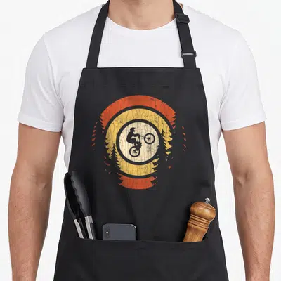 Tablier de cuisine noir avec illustration vintage d'un cycliste sur mountain bike encadré par des arbres et des cercles orange jaunis.