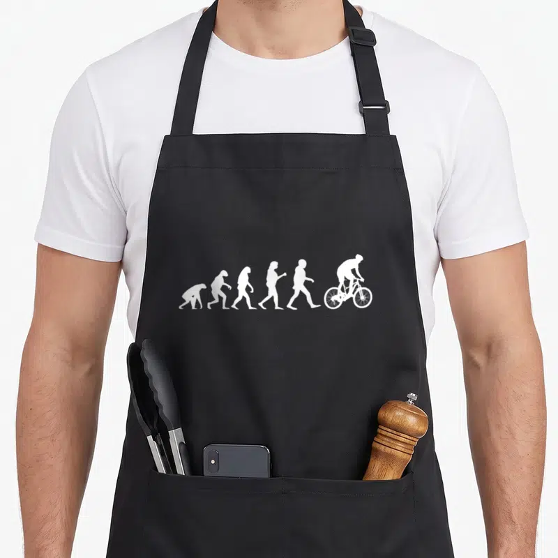 Tablier de cuisine noir avec une illustration blanche représentant l'évolution de l'homme jusqu'au cycliste sur vélo de montagne.