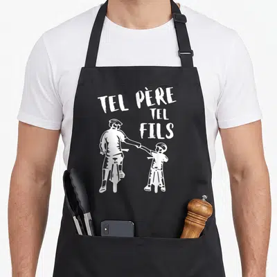 Tablier de cuisine noir avec illustration blanche d'un père et un fils à vélo se tenant la main sous le texte Tel Père Tel Fils.