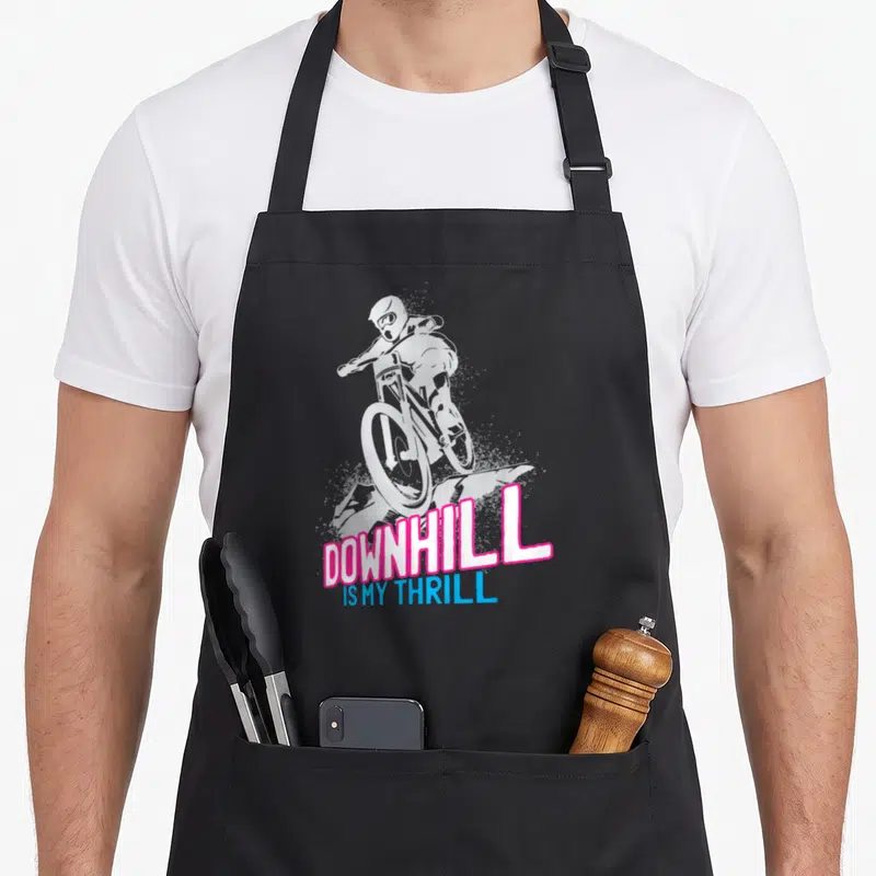 Tablier de cuisine noir avec illustration cycliste en descente et texte DOWNHILL IS MY THRILL en rose et bleu.