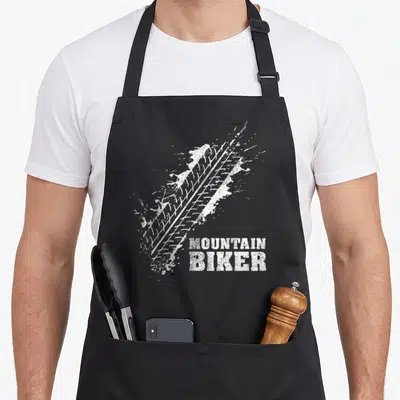 Tablier de cuisine noir avec empreinte de pneu blanche et texte MOUNTAIN BIKER en bas à droite.