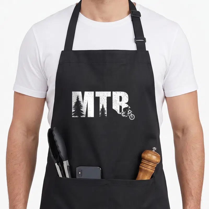 Tablier de cuisine noir avec inscription MTB blanche intégrant des arbres et un cycliste sur sentier.