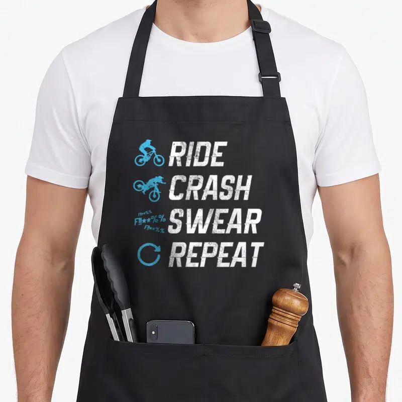 Tablier de cuisine noir avec motif Ride Crash Swear Repeat et silhouettes cyclistes bleues.
