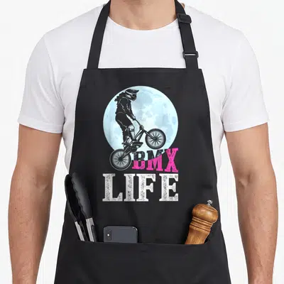 Tablier de cuisine noir avec cycliste BMX effectuant un saut devant une lune bleue et le texte BMX LIFE.