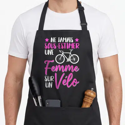 Tablier de cuisine noir avec le texte Ne jamais sous-estimer une femme sur un vélo et un dessin de vélo blanc.