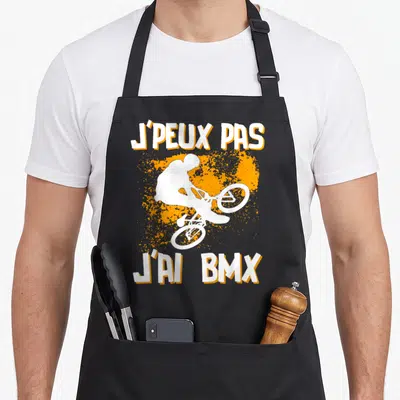 Tablier de cuisine noir avec silhouette cycliste BMX blanche et texte J'peux pas j'ai BMX sur fond orange.