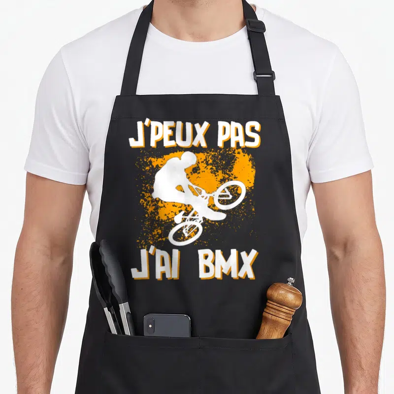 Tablier de cuisine noir avec silhouette cycliste BMX blanche et texte J'peux pas j'ai BMX sur fond orange.