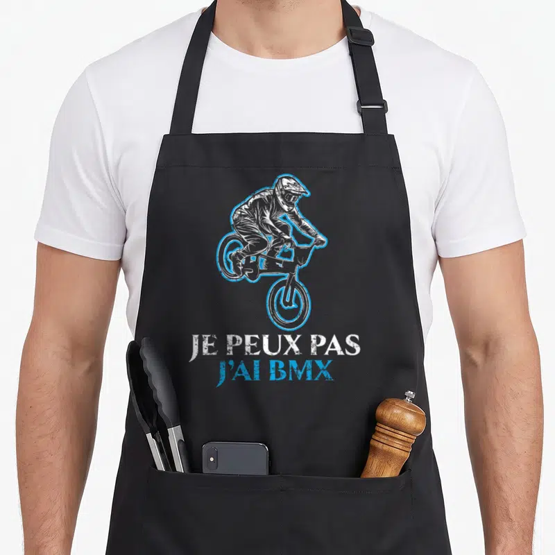 Tablier de cuisine noir avec illustration d'un cycliste BMX effectuant une acrobatie en l'air, souligné par un texte blanc et bleu.