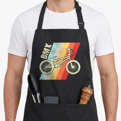 Tablier de cuisine noir avec illustration vintage d'un vélo BMX sur fond de bandes diagonales multicolores et le texte BMX en haut à gauche.