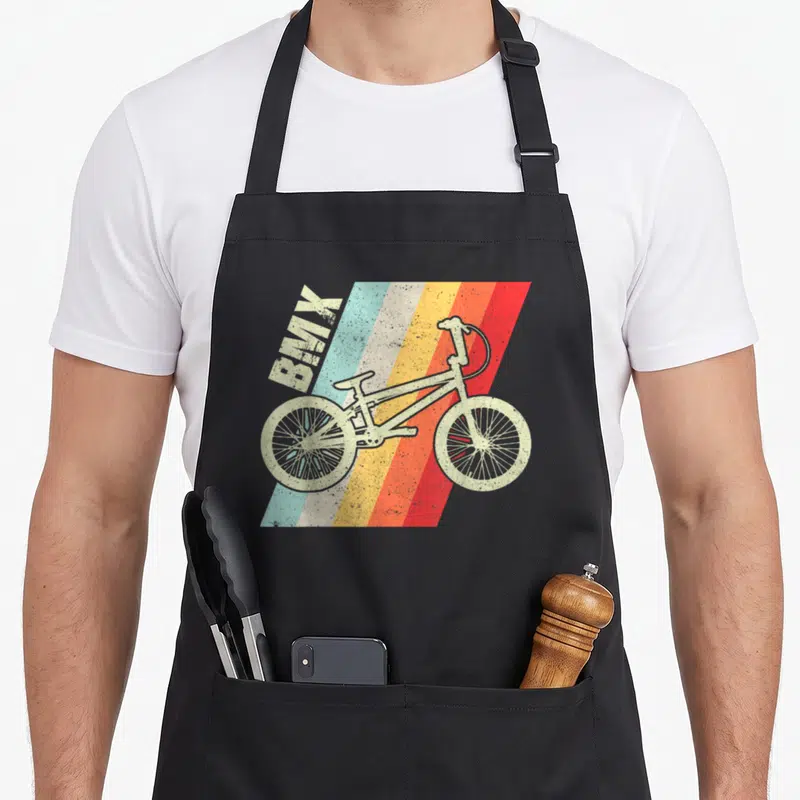 Tablier de cuisine noir avec illustration vintage d'un vélo BMX sur fond de bandes diagonales multicolores et le texte BMX en haut à gauche.