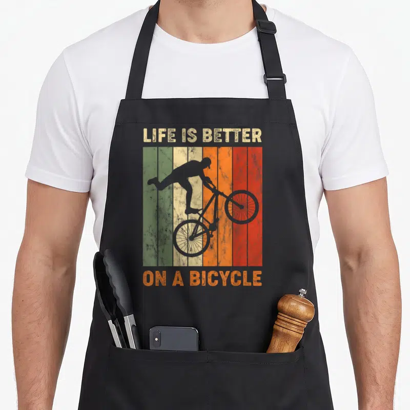 Tablier de cuisine noir avec silhouette de cycliste MTB sur fond de planches vertes, jaunes, oranges et rouges texturées.