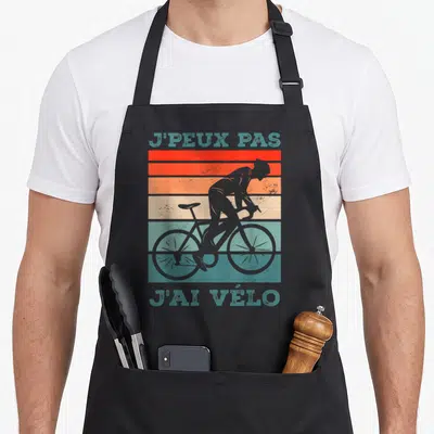 Tablier de cuisine noir avec silhouette cycliste et texte J'peux pas j'ai vélo sur fond de bandes colorées vintage.