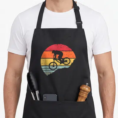 Tablier de cuisine noir avec illustration vintage d'un cycliste en silhouette sur un soleil aux bandes colorées horizontales.