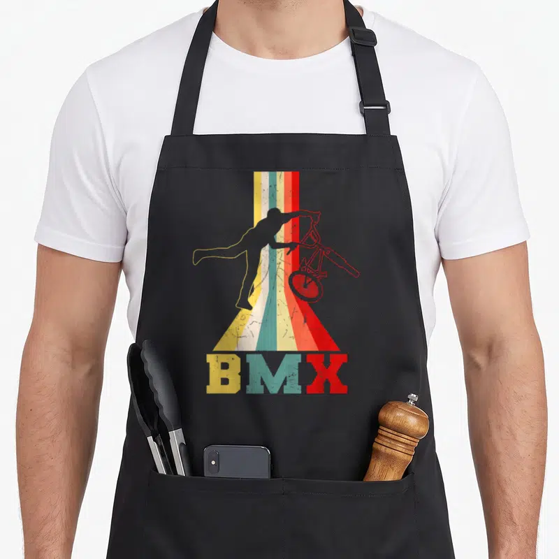 Tablier de cuisine noir avec silhouette cycliste BMX sur fond de bandes verticales colorées et texte BMX en bas.