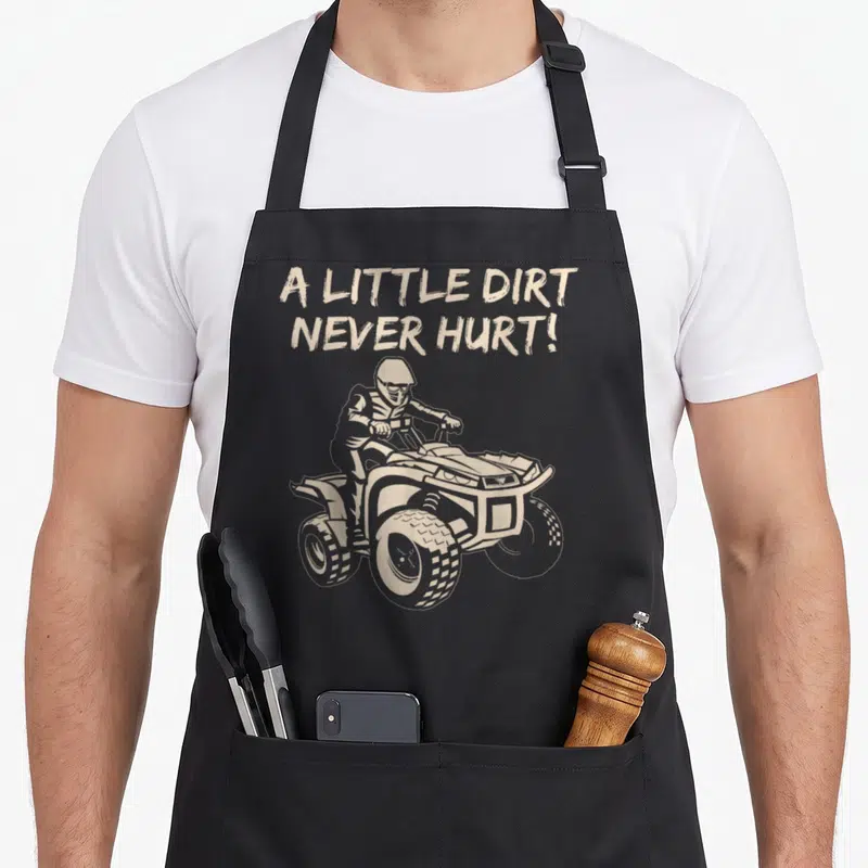 Tablier de cuisine noir avec illustration beige d'un pilote de quad et le texte A little dirt never hurt.