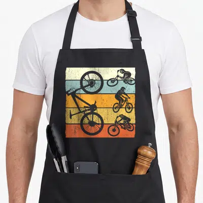 Tablier de cuisine noir avec silhouettes de cyclistes MTB et roues sur fond rayé vintage multicolore.